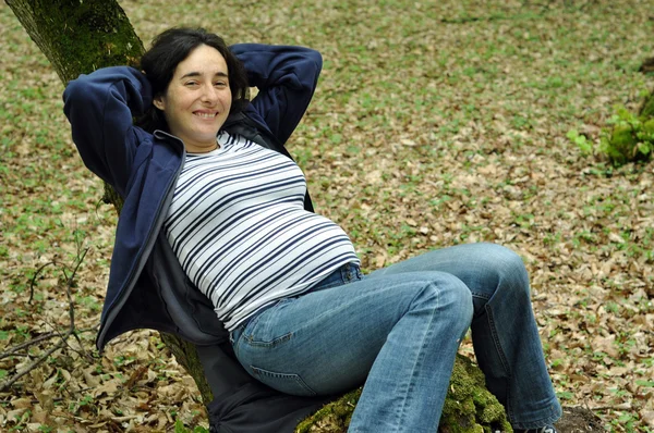 Mujer embarazada relajándose en un tronco de árbol — Foto de Stock