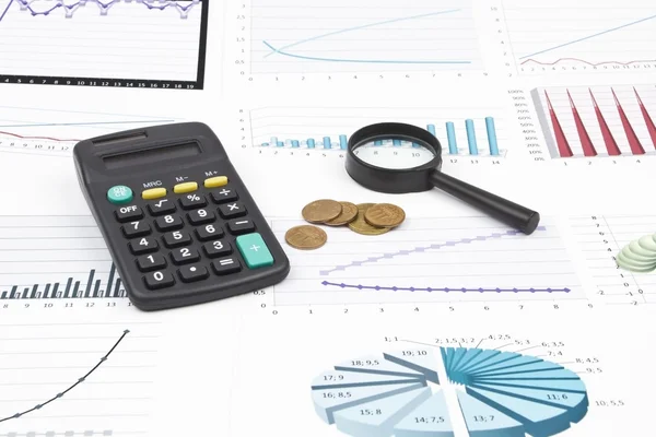 Kalkulator, forstørrelsesfaktor og mynt ligger på forretningskartene – stockfoto
