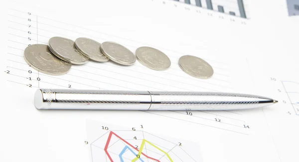 Glanzende pen en munten liggen op de zakelijke grafieken — Stockfoto