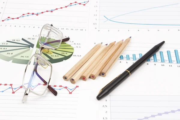 Brillen, zwarte pen en potloden liggen op de zakelijke grafieken — Stockfoto
