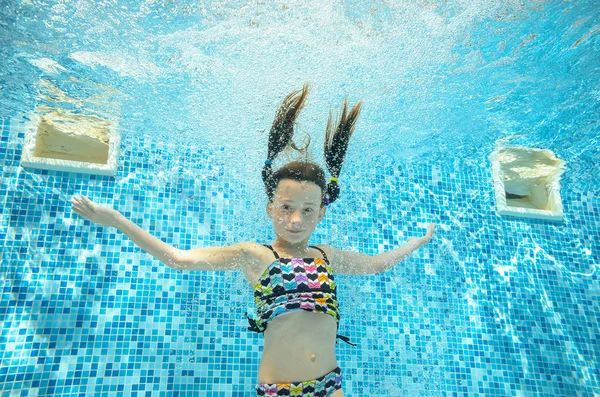Child swims in pool underwater, happy active girl jumps, dives and has fun under water, kid sport on family vacation