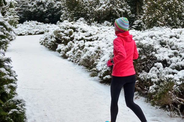 Winter running in park: happy woman runner jogging in snow, outdoor sport and fitness concept