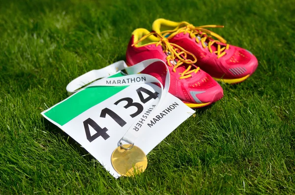 Zapatillas de correr, babero de carrera maratón (número) y medalla de finalizador en el fondo de hierba, deporte, fitness y estilo de vida saludable concepto — Foto de Stock