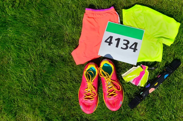 Zapatillas de correr, babero de carrera maratón (número), equipo de corredores y geles de energía sobre fondo de hierba, deporte, fitness y concepto de estilo de vida saludable —  Fotos de Stock