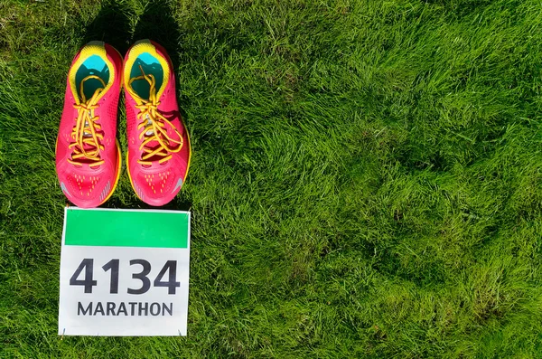 Running shoes and marathon race bib (number) on grass background, sport, fitness and healthy lifestyle concept — Stock Photo, Image