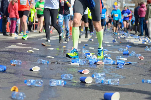 Carrera de maratón, pies de corredores y vasos de agua de plástico en la carretera cerca del punto de refresco, deporte, fitness y el concepto de estilo de vida saludable —  Fotos de Stock