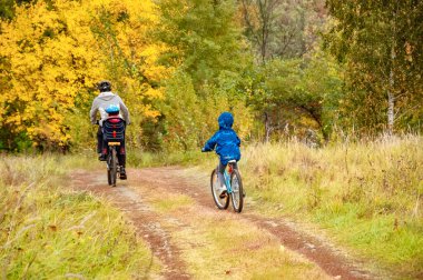 Altın sonbahar parkında aile bisikleti, aktif baba ve çocuklar bisiklet, aile sporu ve açık havada spor yapıyorlar.