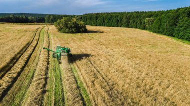 Yukarıdan tarla görüntüsünde çalışan biçerdöver makinesi, olgun buğday tarlalarını hasat eden biçerdöver makinesini birleştirir.