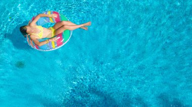 Havuz havuzu manzaralı aktif bir kız, çocuk şişme yüzükle yüzüyor, çocuk aile tatilinde mavi suda eğleniyor.