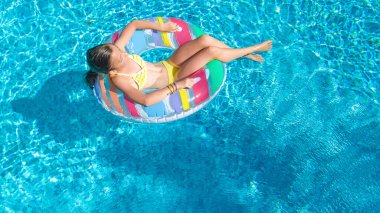 Havuz havuzu manzaralı aktif bir kız, çocuk şişme yüzükle yüzüyor, çocuk aile tatilinde mavi suda eğleniyor.