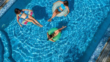 Yüzme havuzundaki aile yukarıdan insansız hava aracı görüntüsü, mutlu anne ve çocuklar şişme halka çöreklerle yüzüyor ve aile tatilinde suda eğleniyor, tatil beldesinde tropikal tatiller