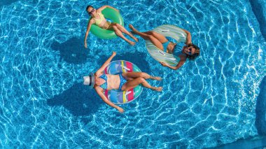 Yüzme havuzundaki aile yukarıdan insansız hava aracı görüntüsü, mutlu anne ve çocuklar şişme halka çöreklerle yüzüyor ve aile tatilinde suda eğleniyor, tatil beldesinde tropikal tatiller