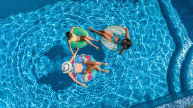 Yüzme havuzundaki aile yukarıdan insansız hava aracı görüntüsü, mutlu anne ve çocuklar şişme halka çöreklerle yüzüyor ve aile tatilinde suda eğleniyor, tatil beldesinde tropikal tatiller