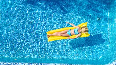 Yüzme havuzunda dinlenen bir kız, şişme yatakta yüzen bir çocuk ve aile tatilinde suda eğlenen bir kız, tropik tatil beldesi, yukarıdan gelen hava aracı manzarası.