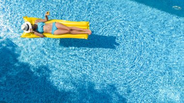 Yüzme havuzunda dinlenen güzel bir genç kız, şişme yatakta yüzen ve aile tatilinde suda eğlenen bir kadın, tropikal tatil beldesi, yukarıdan drone manzarası