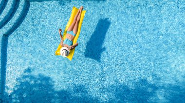 Yüzme havuzunda dinlenen güzel bir genç kız, şişme yatakta yüzen ve aile tatilinde suda eğlenen bir kadın, tropikal tatil beldesi, yukarıdan drone manzarası