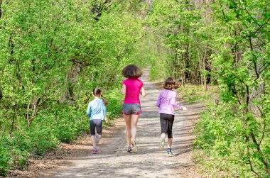 Aile koşusu, mutlu aktif anne ve çocuklar dışarıda koşuyor, çocuklarla ormanda koşuyor, sağlıklı aile sporu ve fitness