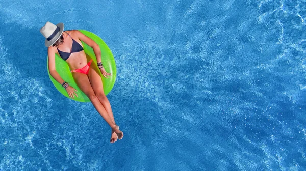Beautiful woman in hat in swimming pool aerial view from above, young girl relaxes and has fun on inflatable ring in water on vacation
