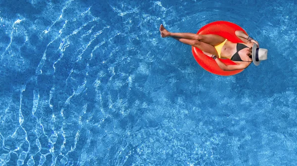 Beautiful woman in hat in swimming pool aerial view from above, young girl relaxes and has fun on inflatable ring in water on vacation