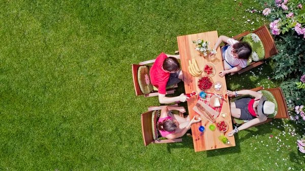 Family and friends eating together outdoors on summer garden party. Aerial view of table with food and drinks from above. Leisure, holidays and picnic concept