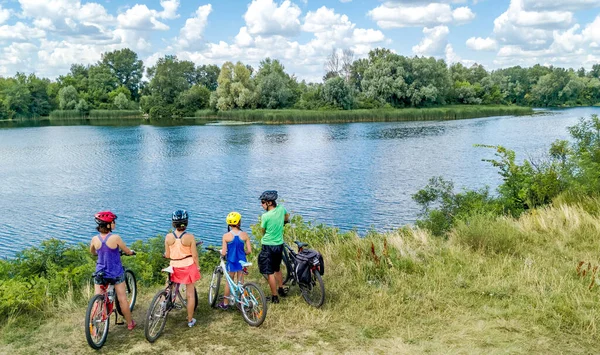 Family on bikes cycling outdoors, active parents and kids on bicycles, aerial view of happy family with children relaxing near beautiful river from above, sport and fitness concept