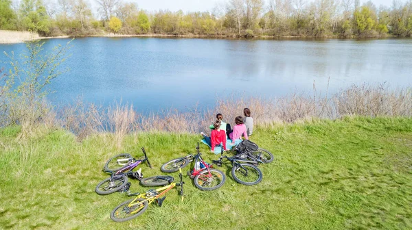 Family on bikes cycling outdoors, active parents and kids on bicycles, aerial view of happy family with children relaxing near beautiful river from above, sport and fitness concept