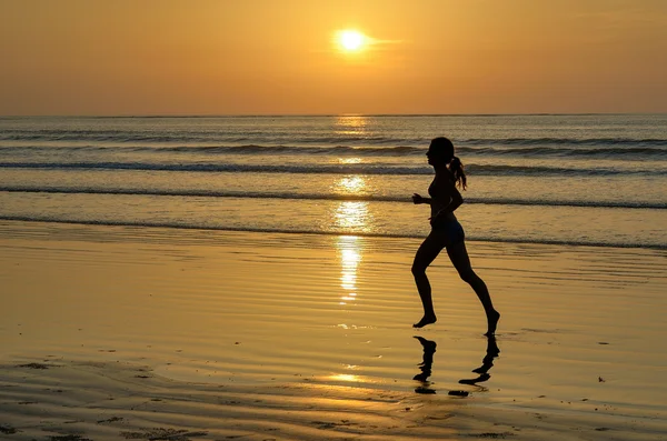 Sylwetka jogger kobieta działa na zachód słońca plaża z odbiciem — Zdjęcie stockowe