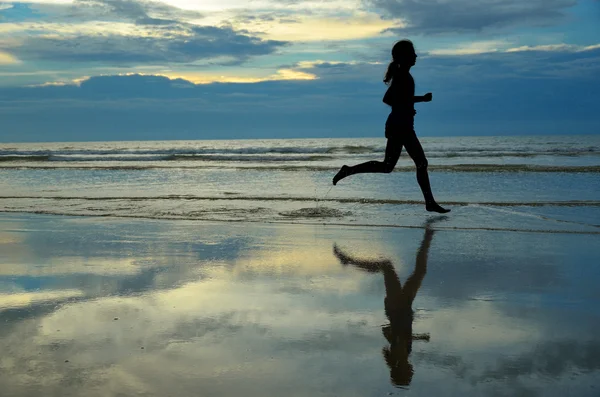 Silhouette einer Joggerin, die am Strand bei Sonnenuntergang mit Spiegelung läuft — Stockfoto