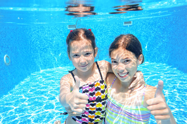 Happy children swim in pool underwater, girls swimming