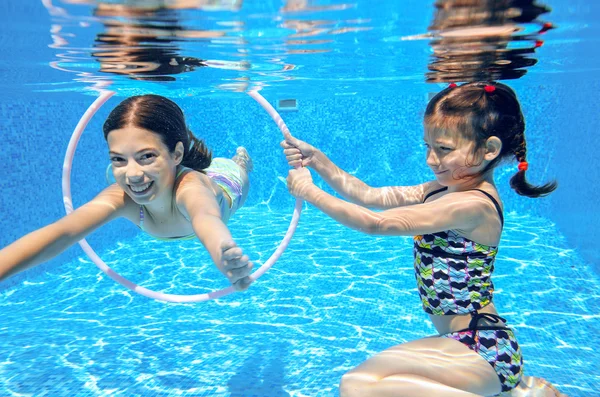 Niños felices nadan en la piscina bajo el agua, niñas nadando, jugando y divirtiéndose, niños deportes acuáticos —  Fotos de Stock