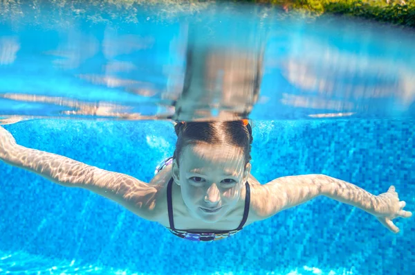 Счастливая девочка плавает в бассейне под водой, активный ребенок плавает, играет и развлекается, детский водный спорт — стоковое фото