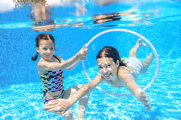 Happy children swim in pool underwater, girls swimming, playing and having fun, kids water sport