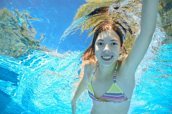 Child swims in pool underwater, happy active girl has fun in water, kid sport on family vacation