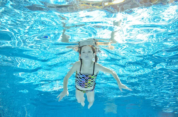 Child swims in pool underwater, happy active girl has fun in water, kid sport on family vacation