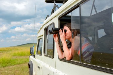 Afrika 'da safari yapan bir kadın, Kenya' da geziyor, vahşi hayatı dürbünle izliyor.