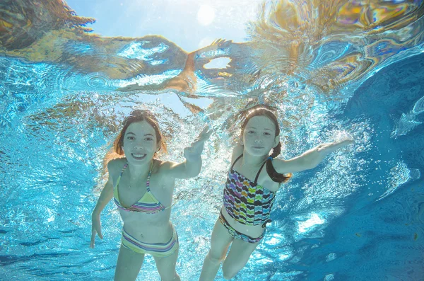 Children swim in pool underwater, happy active girls have fun in water