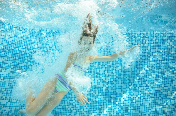 Girl jumps and swims in pool underwater, happy active child has fun in water, kid sport on family vacation