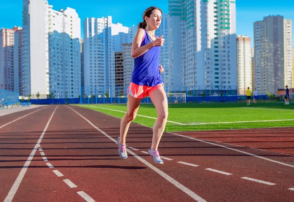 Счастливая активная женщина, бегущая по дорожке, бегущая и тренирующаяся на стадионе, спорт и фитнес в городе, городской фон — стоковое фото