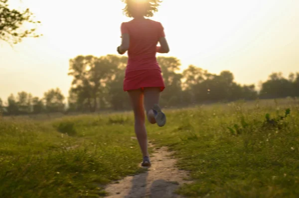 Blurred background: woman runner running on rural road on sunset or sunrise, sport and fitness concept — Stock Photo, Image