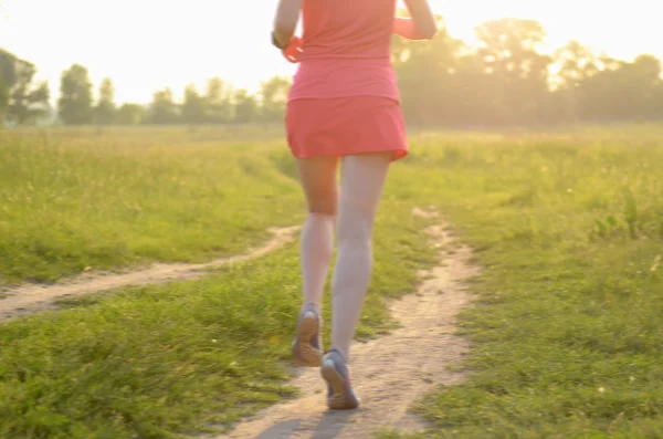 Unscharfer Hintergrund: Läuferin läuft bei Sonnenuntergang oder Sonnenaufgang auf Landstraße, Sport- und Fitnesskonzept — Stockfoto