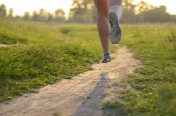 Fundo desfocado: mulher corredor correndo na estrada rural no pôr do sol ou nascer do sol, esporte e conceito de fitness — Fotografia de Stock