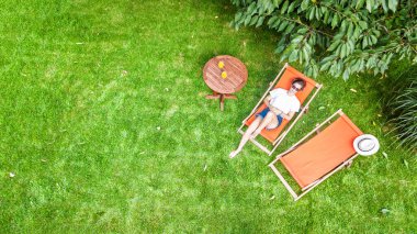 Genç kız yaz bahçesinde dinleniyor güneş paneli çimenlerin üzerinde dinleniyor, haftasonu yeşil parkta dinleniyor, yukarıdan insansız hava aracı görüşü var.