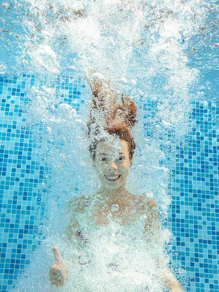 Girl jumps and swims in pool underwater, happy active child has fun in water, kid sport on family vacation