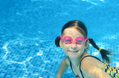 Child swims in pool underwater, happy active girl in goggles has fun under water, kid sport on family vacation