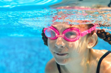 Child swims in pool underwater, happy active girl in goggles has fun under water, kid sport on family vacation