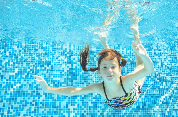 Girl jumps, dives and swims in pool underwater, happy active child has fun under water, kid sport on family vacation