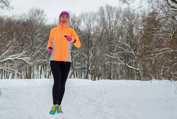 Winter running in forest: happy woman runner jogging in snow, outdoor sport and fitness concept