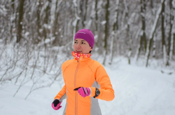 Winter running in forest: happy woman runner jogging in snow, outdoor sport and fitness concept Stock Image