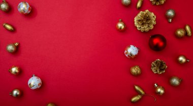 Kenarlarında Noel süsleri olan kırmızı bir arkaplan. Altın, kırmızı ve beyaz mücevherler, çam kozalakları ve fındıklar kopya alanı ile şenlik çerçevesi oluşturuyorlar..