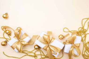 Beyaz hediyeler, altın fiyonklar ve bej arka planda ışıldayan süslemelerle süslü bir kış düzeni. Tebrik kartları, web pankartları ya da markalar için mükemmel.